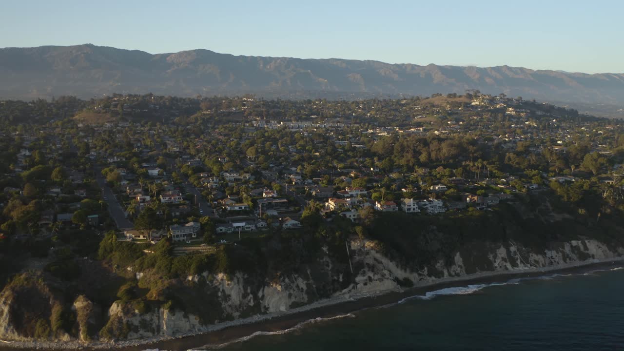 무인 항공기는 여름날 해안 캘리포니아 마을을 향해 날아가고 배경에는 산이 있습니다.