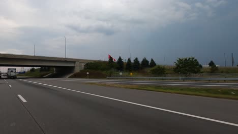 car pov: carretera canadiense con un asta de bandera que ondea la bandera nacional en el borde de la carretera
