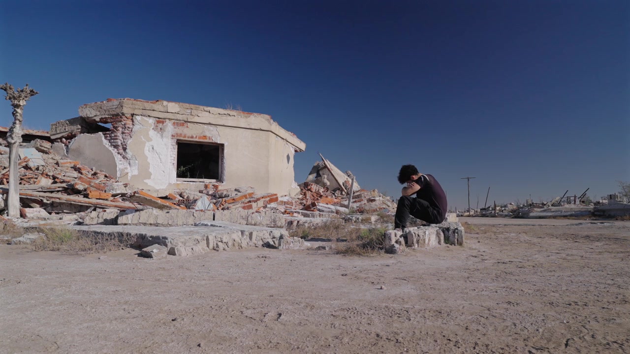 Persona accanto a strutture crollate tiene la testa tra le mani in angoscia e tristezza per la devastazione delle rovine abbandonate, medium statico.
