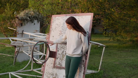 woman touches old basketball hoop. vintage broken item for playing sports game. depressed female in alone feels useless and devastation at sunset