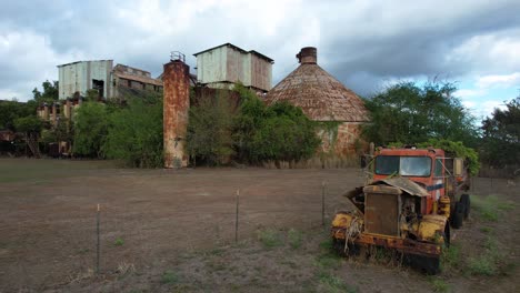 Old-truck-with-abandoned-Koloa-sugar-mill-Kauai,-Hawaii-in-background,-circle-drone-shot