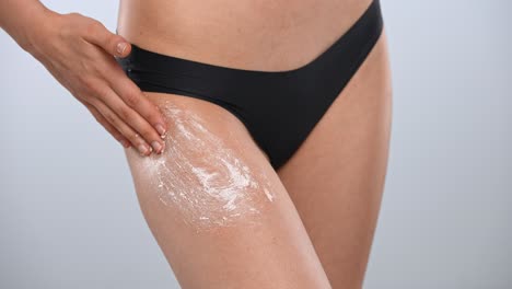 fashionable black bikini on woman with blue background a woman in a stylish black bikini rubs a scrub on her leg against a bright blue background demonstrating elegance and confidence close up