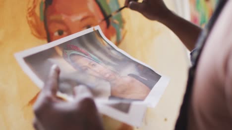 mid section of male artist painting on canvas looking at portrait on paper at art studio