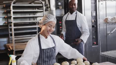 Happy-diverse-bakers-working-in-bakery-kitchen,-holding-baking-sheet-with-rolls-in-slow-motion