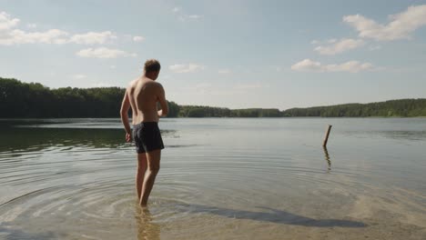 adult guy standing on lakeshore throwing stone in peaceful water of jezioro glebokie, poland