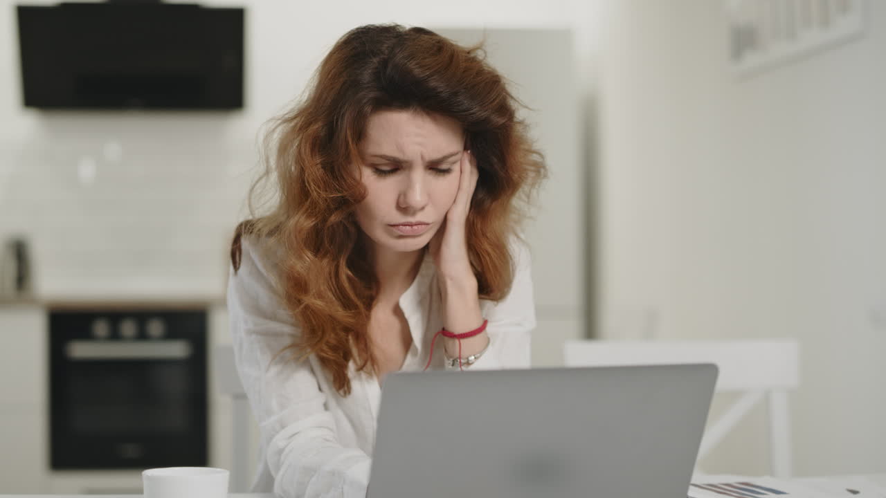 mujer frustrada trabajando en la computadora en casa. mujer joven mirando la computadora portátil en la cocina.
