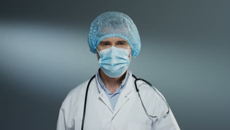 portrait shot of the handsome man doctor in blue hat taking off mask from his mouth and smiling cheerfully to the camera