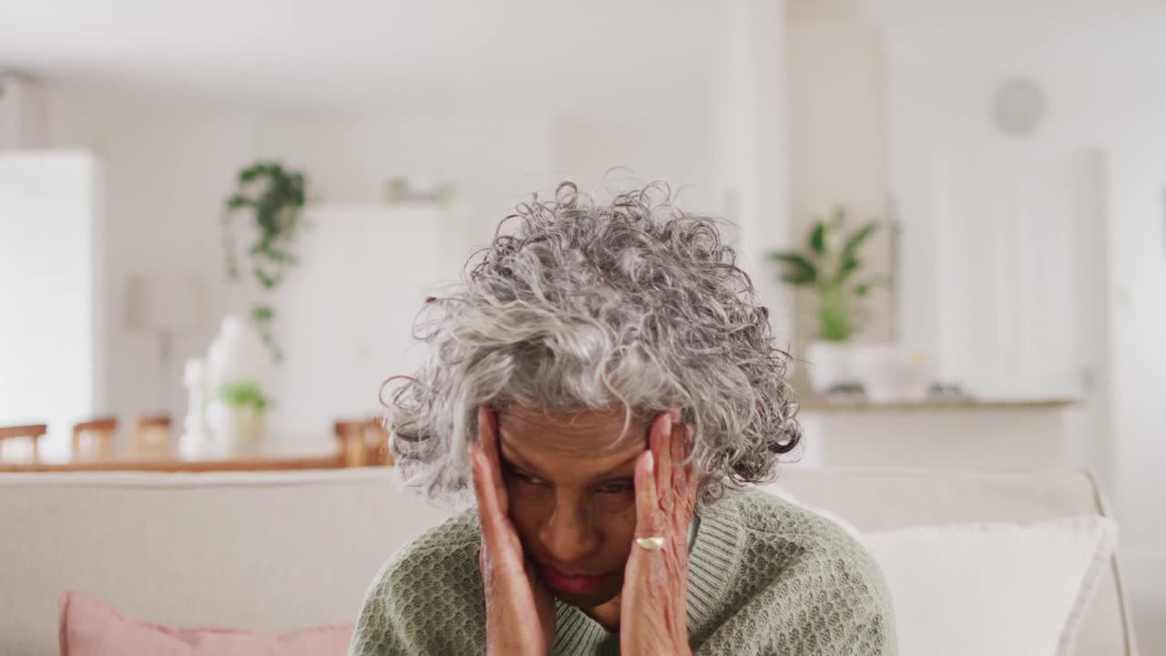 retrato de una anciana afroamericana cansada sentada en el sofá, sosteniendo su cabeza