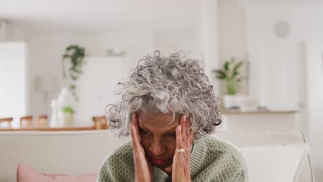 portrait of tired senior african american woman sitting on sofa, holding her head