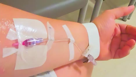 una persona blanca caucásica de piel oliva recibe un acceso por vía intravenosa para que los profesionales médicos accedan fácilmente, ya que su brazo izquierdo está conectado a un examen único en una bata de paciente