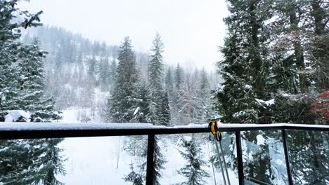 Timelapse-of-a-snowfall-in-a-pine-forest-in-Revelstocke,-British-Columbia,-Canada-with-a-pair-of-ski-poles-lying-on-a-glass-railing