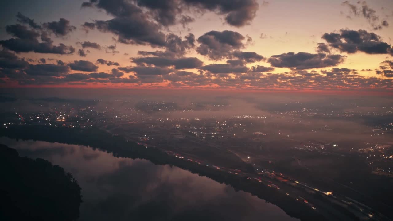 A breathtaking cityscape captured at dusk (or dawn), featuring a glowing horizon painted in vivid shades of orange and red beneath a canopy of dark, moody clouds