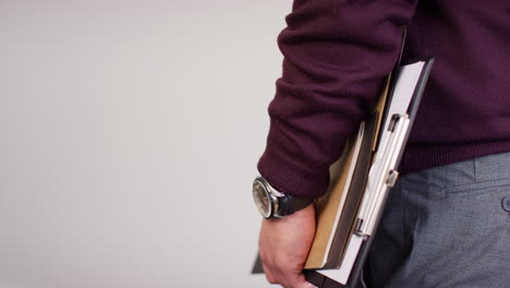 fotografía de estudio de cerca de un maestro masculino contra un fondo blanco sosteniendo carpetas bajo el brazo