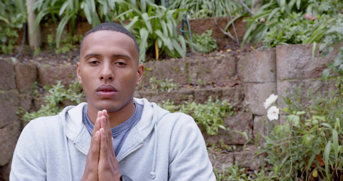 African American man sitting in terraced yard holding hands in prayer, breathing and opening eyes