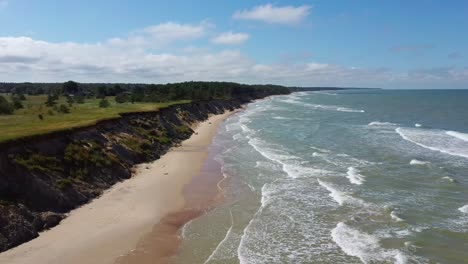 Flying-Over-Coastline-Baltic-Sea-Ulmale-Seashore-Bluffs-Near-Pavilosta-Latvia-and-Landslides-With-an-Overgrown,-Rippling-Cave-Dotted-Cliff-and-Pebbles