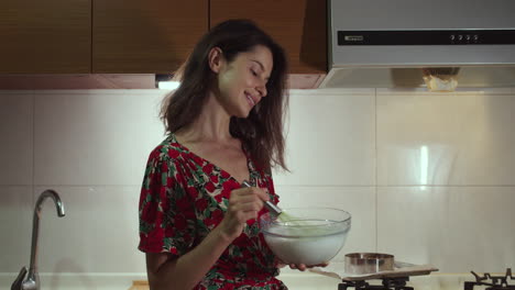 mujer sonriendo y mezclando manualmente la masa con batidor en la cocina