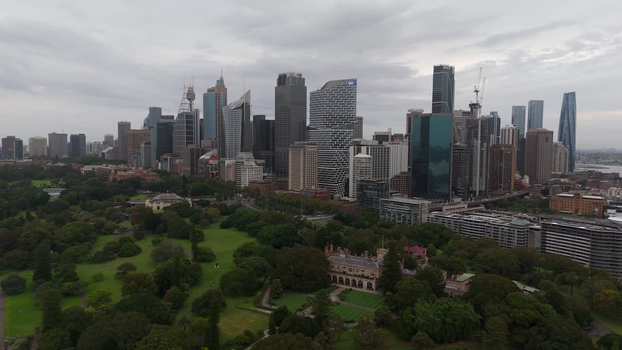 Aerial establishing shot of Royal Botanic Garden with skyline Skyscrapers of Sydney, Australia. Cloudy day with dark sky in Australia. Wide shot.