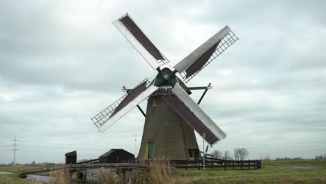 Windmill-in-Dutch-lowland-wetlands-with-bikes-cycling-past,-camera-still-shot
