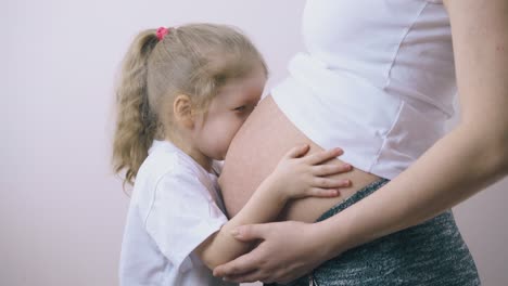 chica alegre besa el vientre grande de la mamá embarazada en la habitación