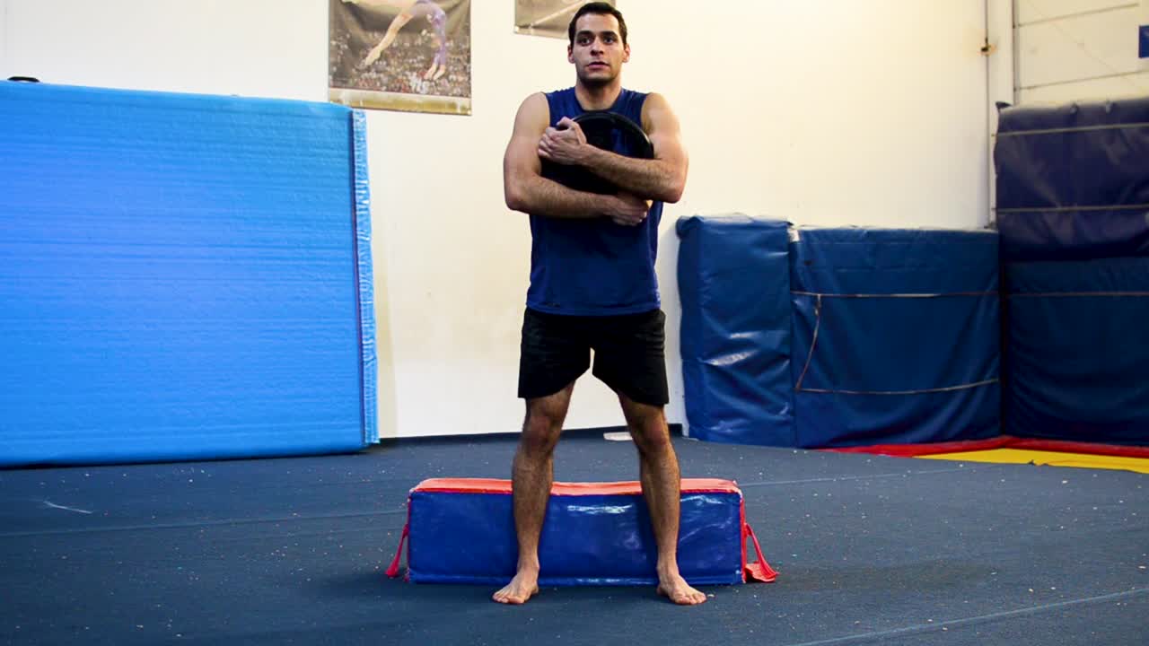 정면에서 가중 스쿼트를 하는 체조 체육관에 있는 남자의 스틸 샷