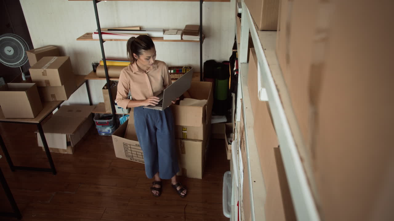 Female Manager with Laptop Checking Parcels in Storage Office