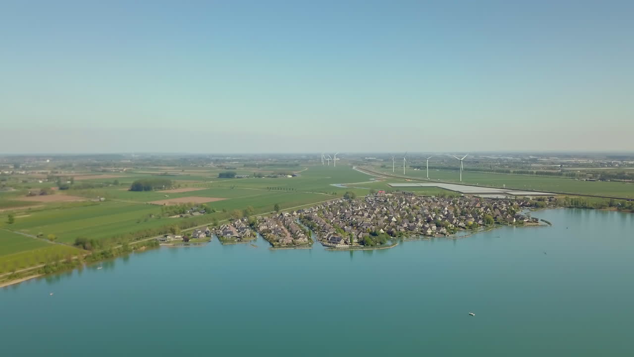 Aerial drone shot over the lake revealing the suburban and flat landscape with windmills in the Netherlands, Europe.