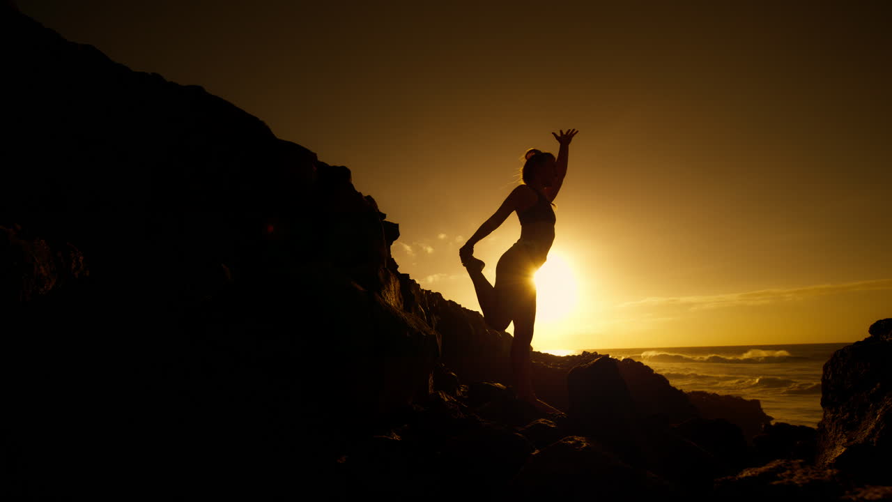 Woman practicing yoga at sunset on a rocky beach