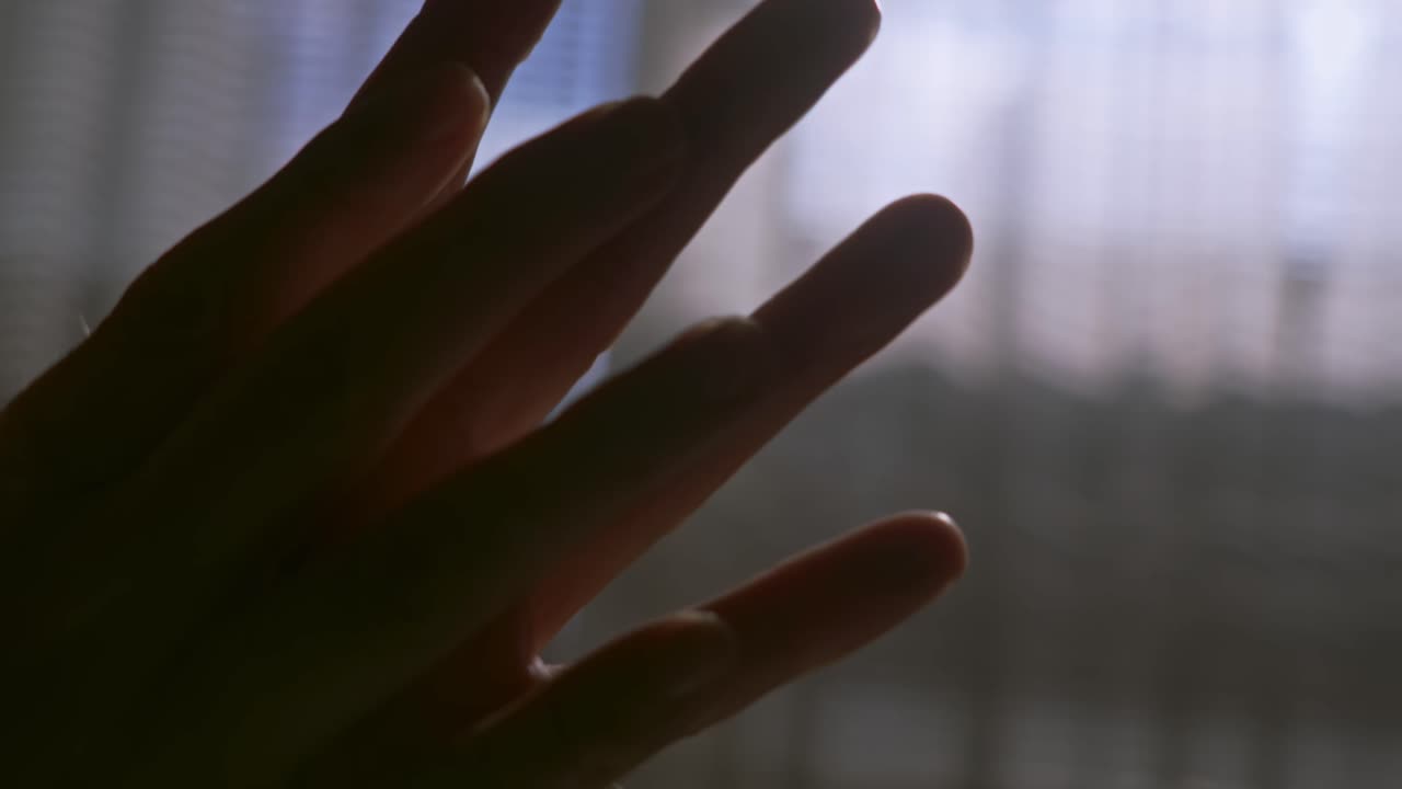 Fingers clasp in emotional gesture in moody room shadows close-up