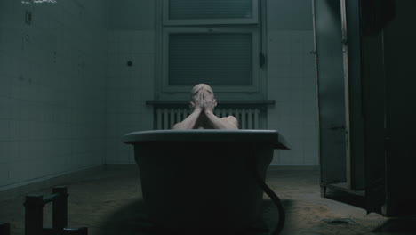 pale bald skinny man takes a bath in the creepy old bathroom at night