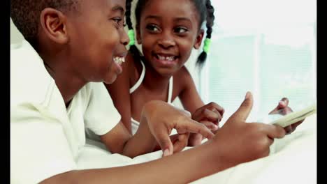 cute siblings using tablet in bed