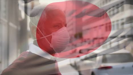 Animation-of-flag-of-japan-waving-over-caucasian-man-wearing-face-mask-in-city-street