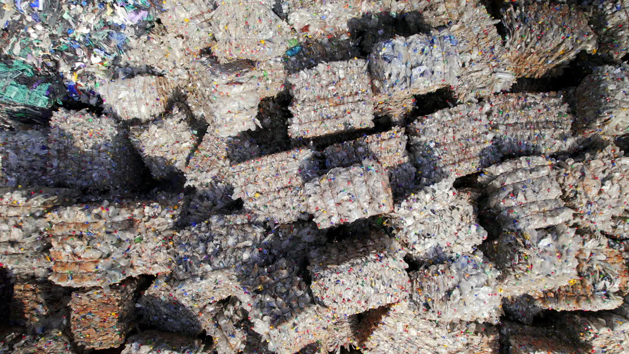Multiple cubes of compressed transparent plastic garbage at waste recycling factory in open air