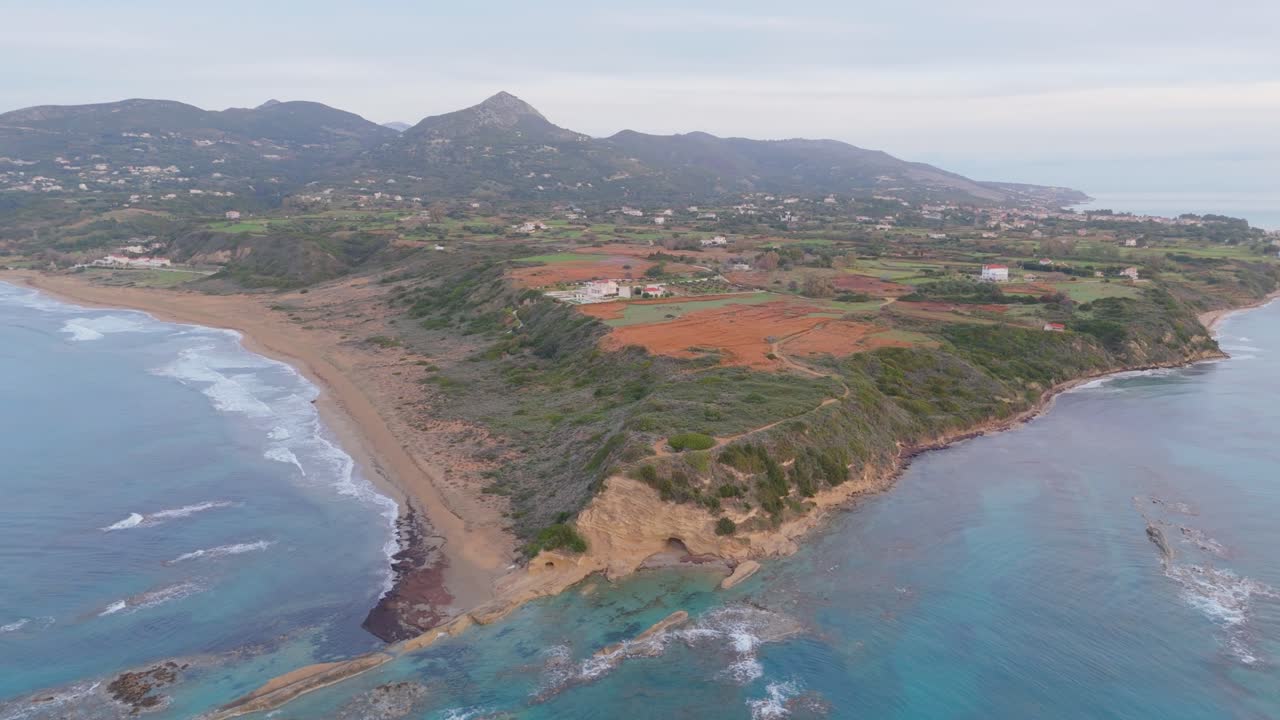 Reverse drone flight over Kefalonia coastline near Skala, moving inland over cliffs, beach, and terraced fields at golden hour.