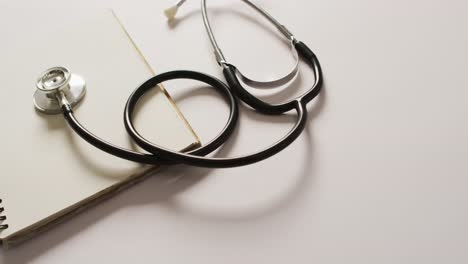 Video-of-close-up-of-stethoscope-with-notebook-on-pink-background