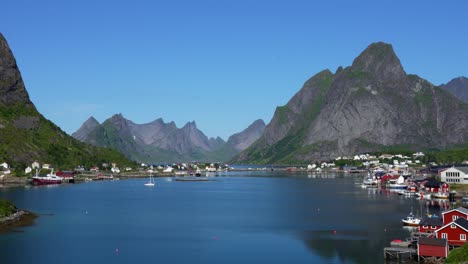 The-city-of-Reine-with-mountain-peaks-behind-it-on-a-sunny-Summer-day-in-Lofoten,-Norway