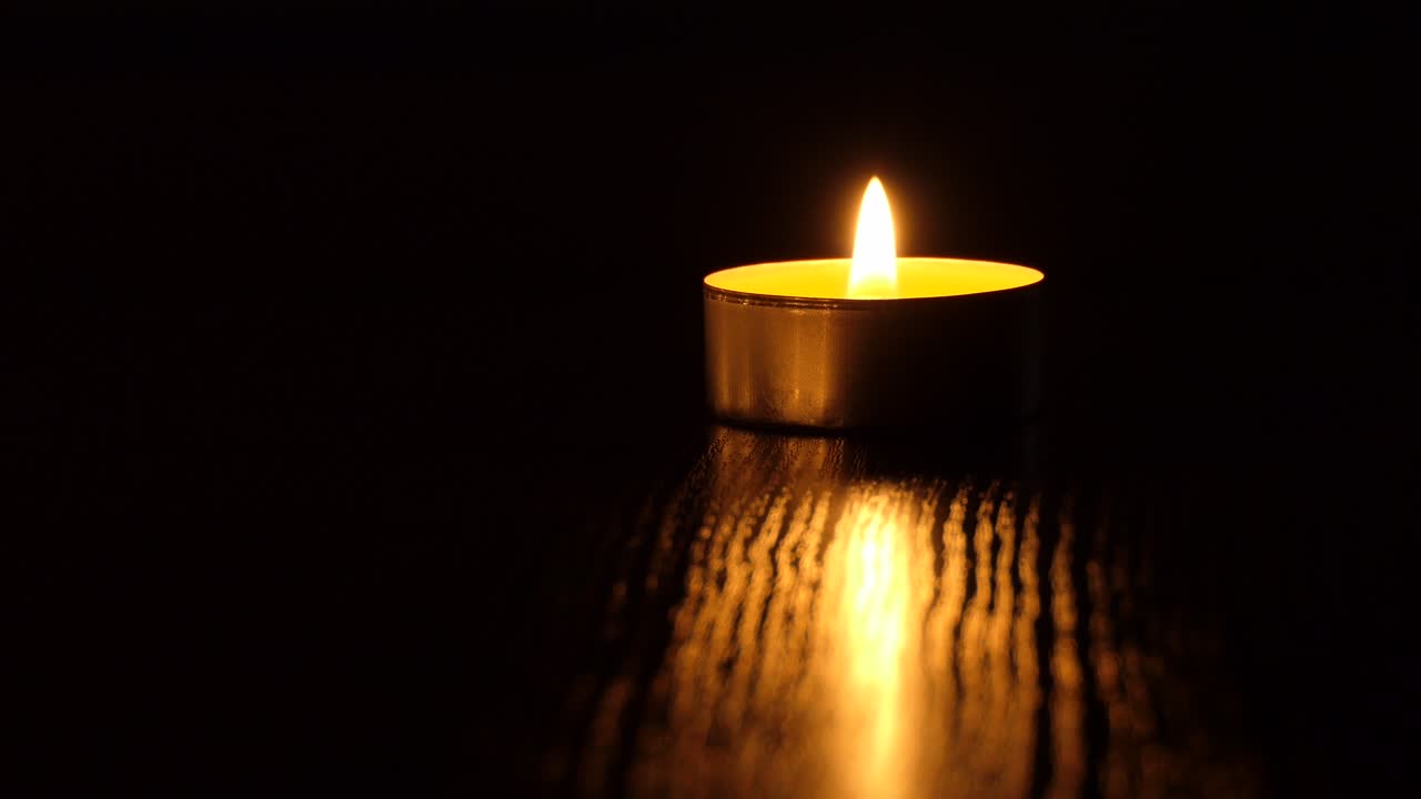 La candela tremola nel buio. Una candela bianca e rotonda brucia su uno sfondo scuro. Candele rotonde bruciano e si spengono. Dolore. Romanticismo. Gioia. Video 4K.