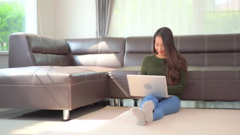 While-sitting-on-the-floor,-an-attractive-young-woman-works-on-her-laptop