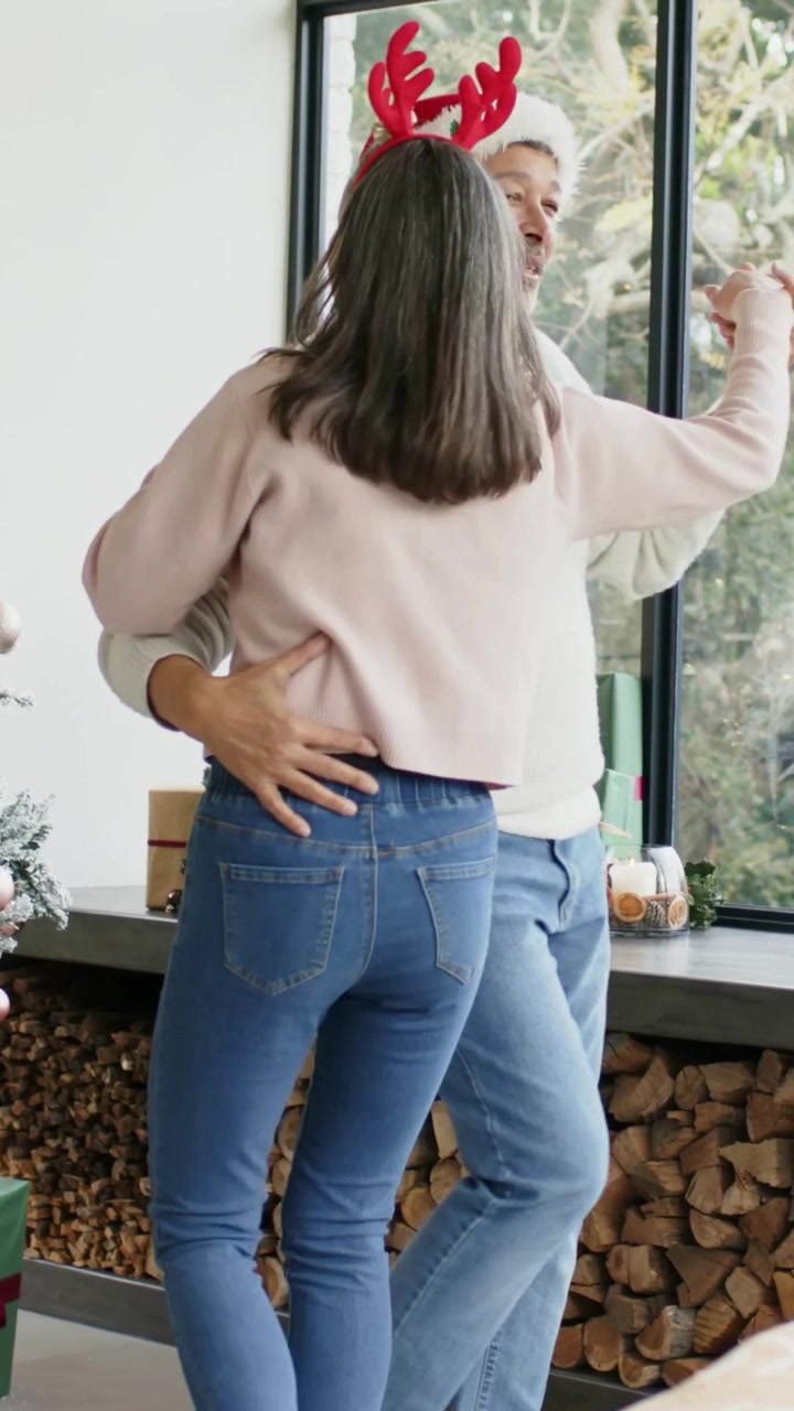 Video verticale: Donna che si muove esortando un uomo con un cappello da Babbo Natale, tenendosi per mano e dondolando vicino all'albero di Natale a casa.