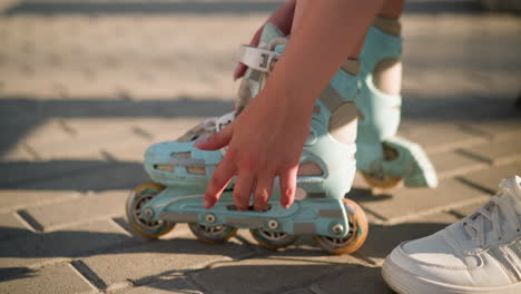 side view of individual adjusting strap on roller skate of left leg, ensuring secure fit, hand focusing on buckle under sunlight, with slight movement, partially visible white sneakers