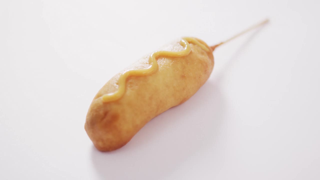 Video of corn dog with mustard on a white surface