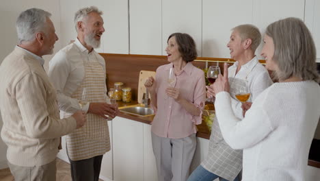 Group-Of-Cheerful-Senior-Friends-Talking-And-Laughing-While-Drinking-Wine-In-The-Kitchen-1