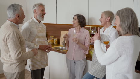 group of cheerful senior friends talking and laughing while drinking wine in the kitchen 1