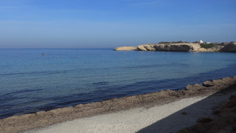 calm tunisian beach with clear water and a rocky shoreline under a bright blue sky