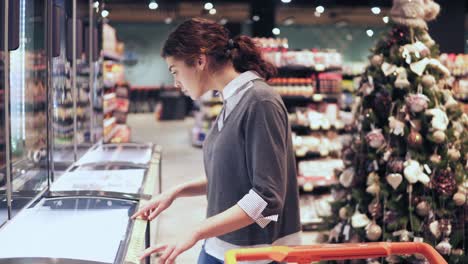 Junges-Brünettes-Mädchen-Nimmt-Eine-Packung-Butter-Aus-Dem-Gefrierschrank.-Einkaufen-Im-örtlichen-Lebensmittelgeschäft