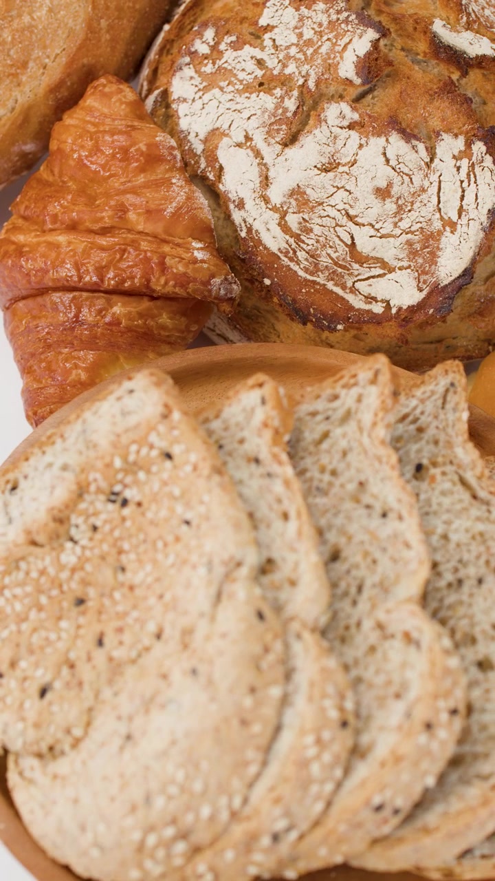 Panoramica ravvicinata di pane multicereale a fette, croissant e pagnotte di pane a lievitazione naturale su sfondo bianco.