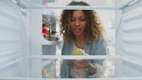 mujer decepcionada mirando dentro del refrigerador vacío excepto por la patata en el estante