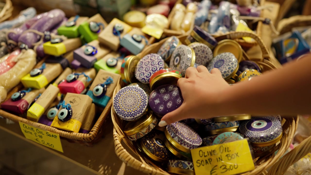 Primo piano della mano di un turista che sceglie una scatola di latta decorata con sapone all'olio d'oliva in un negozio di souvenir greco