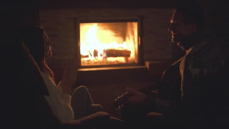 the man with woman playing guitar near the fireplace