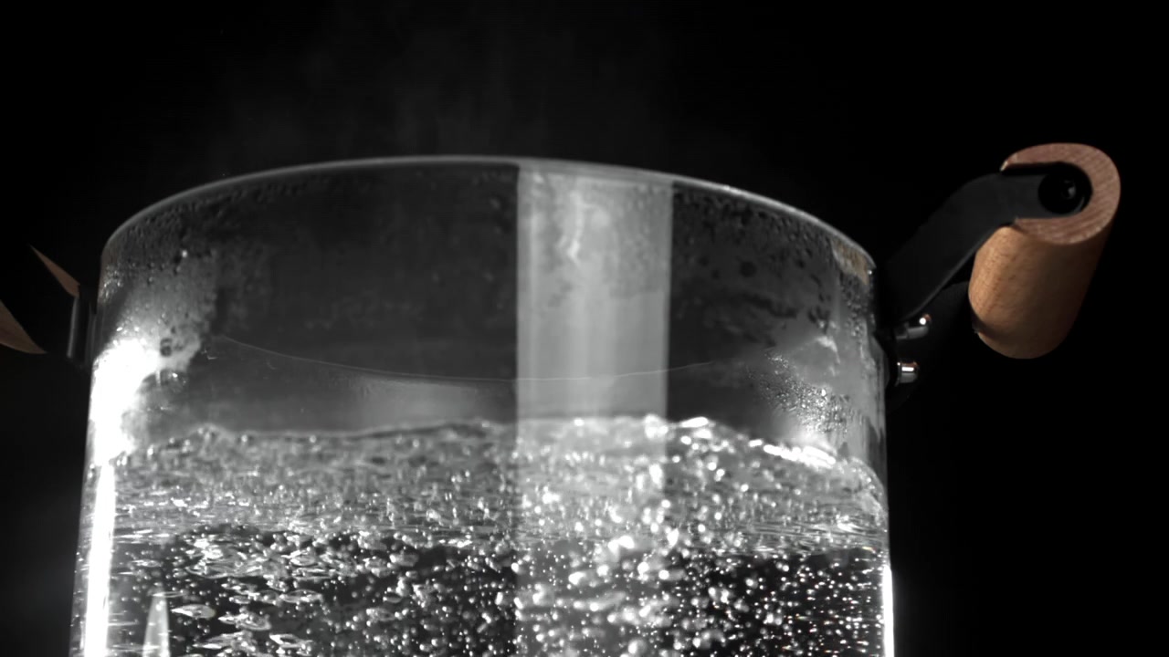 Primo piano di acqua bollente con bolle e vapore in una pentola di vetro