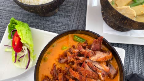 Traditionelles-Thailändisches-Rotes-Curry-Knusper-Entengericht-Und-Grünes-Curry-Hähnchen-Mit-Reis-In-Einer-Kokosnussschale,-Restaurant-Mit-Thailändischer-Küche,-4K-Aufnahme